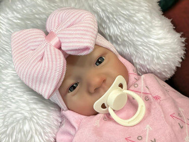 A baby wearing a pink outfit is comfortably lying on a blanket, surrounded by a serene atmosphere.